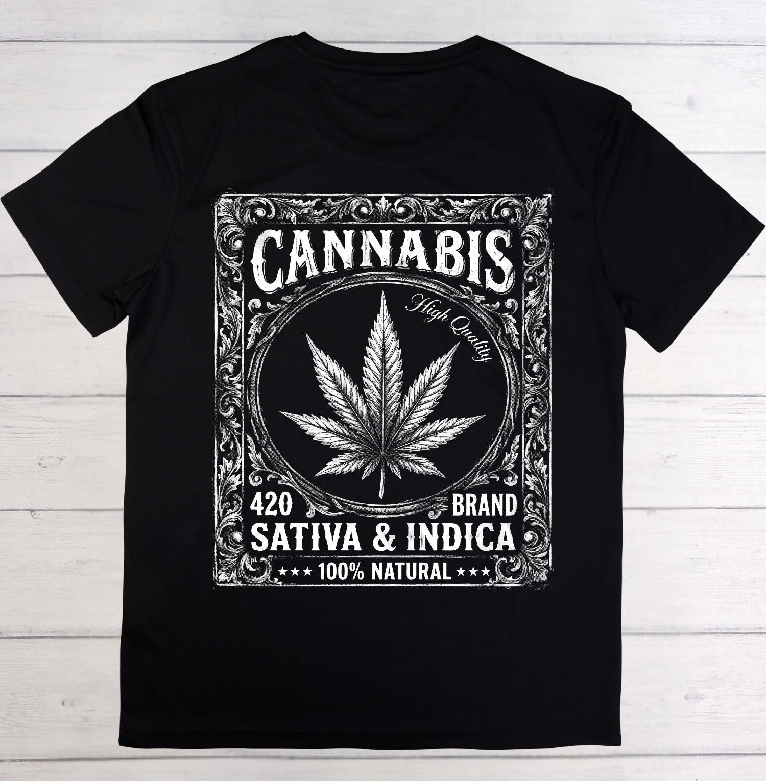 A black short-sleeve crewneck t-shirt laid flat on a white wood plank background. The front features a large white graphic print styled like a vintage ornate label, containing a cannabis leaf, the word 'CANNABIS', 'High Quality', '420 BRAND', 'SATIVA & INDICA', and '100% NATURAL'.
