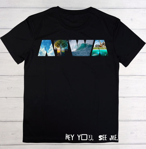 A black short-sleeve t-shirt laid flat on a white wood plank background. The front features a graphic spelling 'NOLA' in stylized letters filled with scenic images of New Orleans, and the text 'HEY YOU, SEE ME,' is printed in white near the bottom hem.