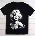 A black short-sleeve t-shirt featuring a large white graphic print of Marilyn Monroe on the front, laid flat on a light-colored wooden plank background.