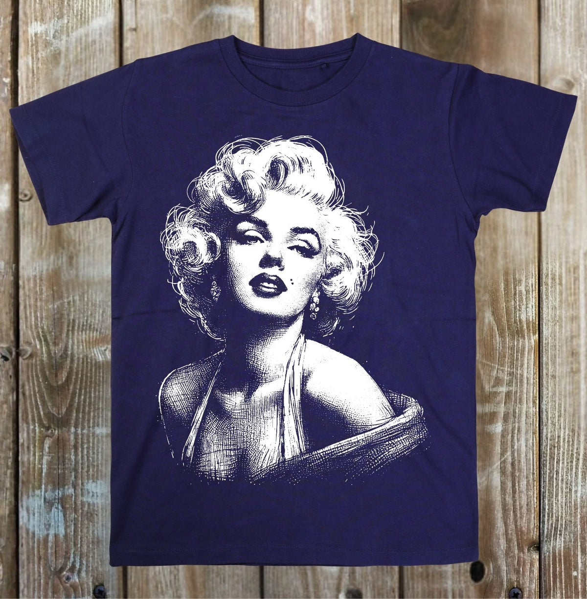 A navy blue short-sleeve t-shirt featuring a white graphic print of Marilyn Monroe, displayed flat against a rustic wooden plank background.