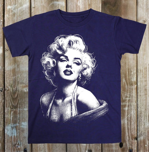 A navy blue short-sleeve t-shirt featuring a white graphic print of Marilyn Monroe, displayed flat against a rustic wooden plank background.