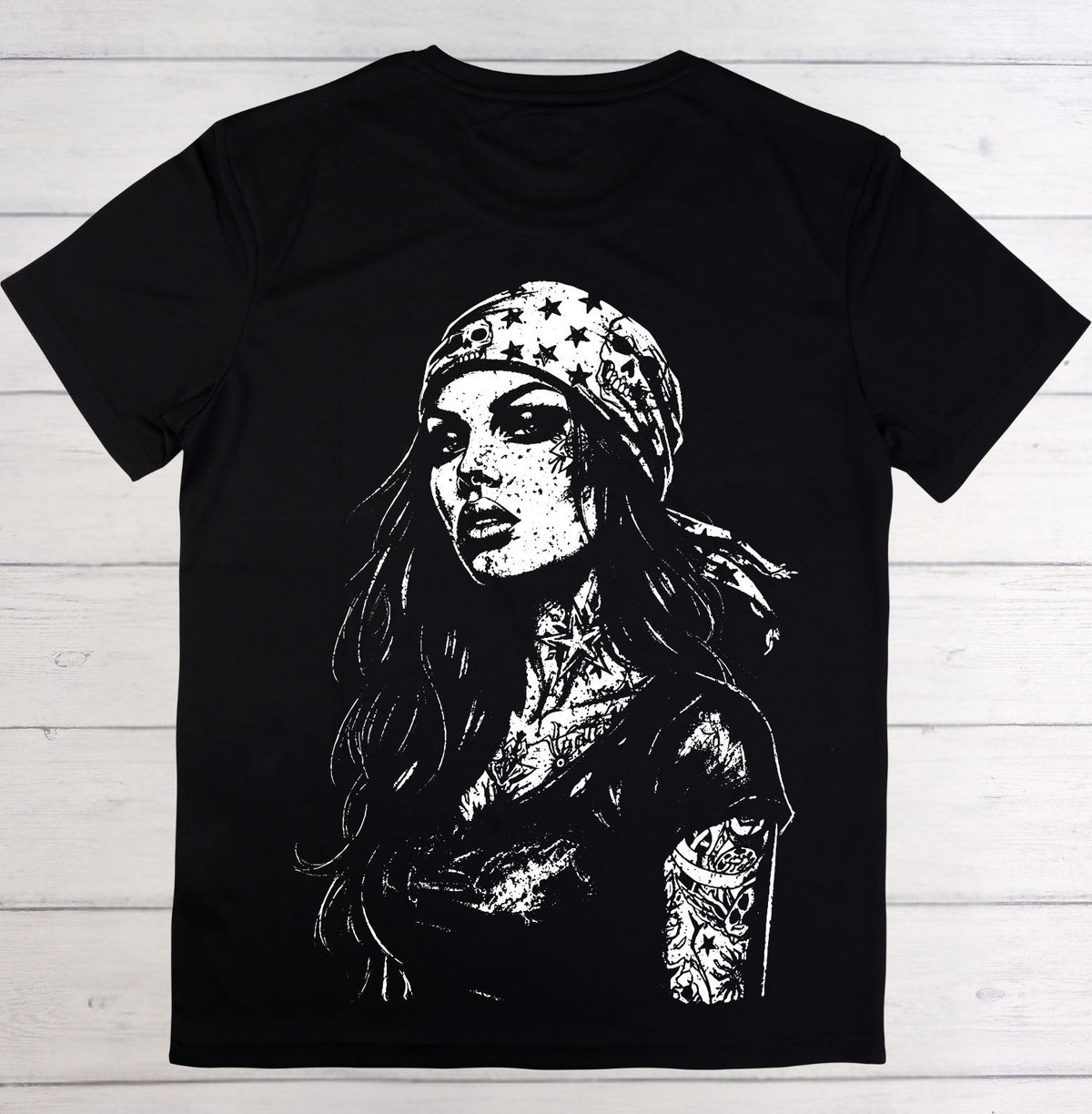 A black short-sleeve crewneck t-shirt featuring a large white graphic print of a woman with a bandana decorated with stars, laid flat on a white wood plank background.