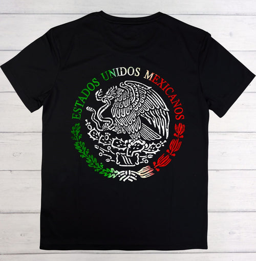 A black short-sleeve t-shirt laid flat on a white wood plank background, featuring a large circular Mexican emblem graphic on the chest with the words 'ESTADOS UNIDOS MEXICANOS' in green, white, and red.