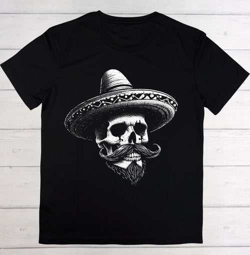 A black short-sleeve crewneck t-shirt featuring a detailed white graphic of a skull wearing a sombrero and a large mustache, laid flat on a light-colored wooden plank background.
