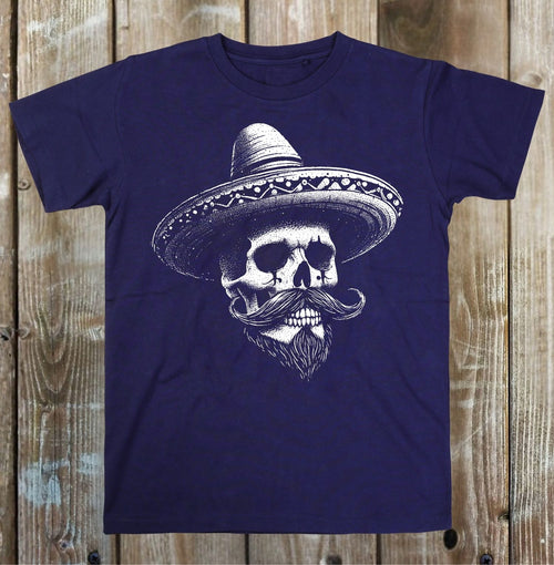 A navy blue short-sleeve t-shirt with a white graphic of a skull wearing a sombrero and a mustache, displayed flat against a rustic wooden plank background.