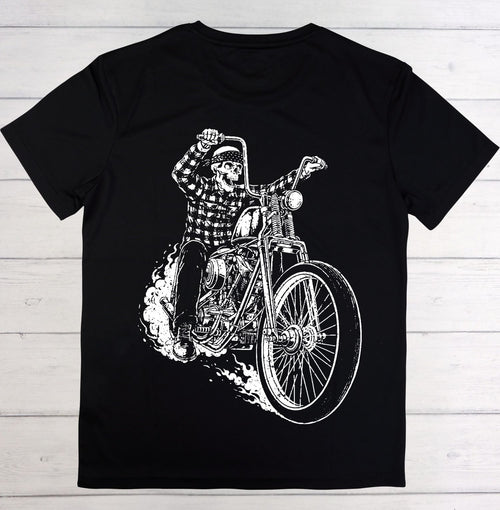 A black short-sleeve crewneck t-shirt featuring a large white graphic print of a skeleton riding a chopper motorcycle, laid flat on a light gray wood plank background.
