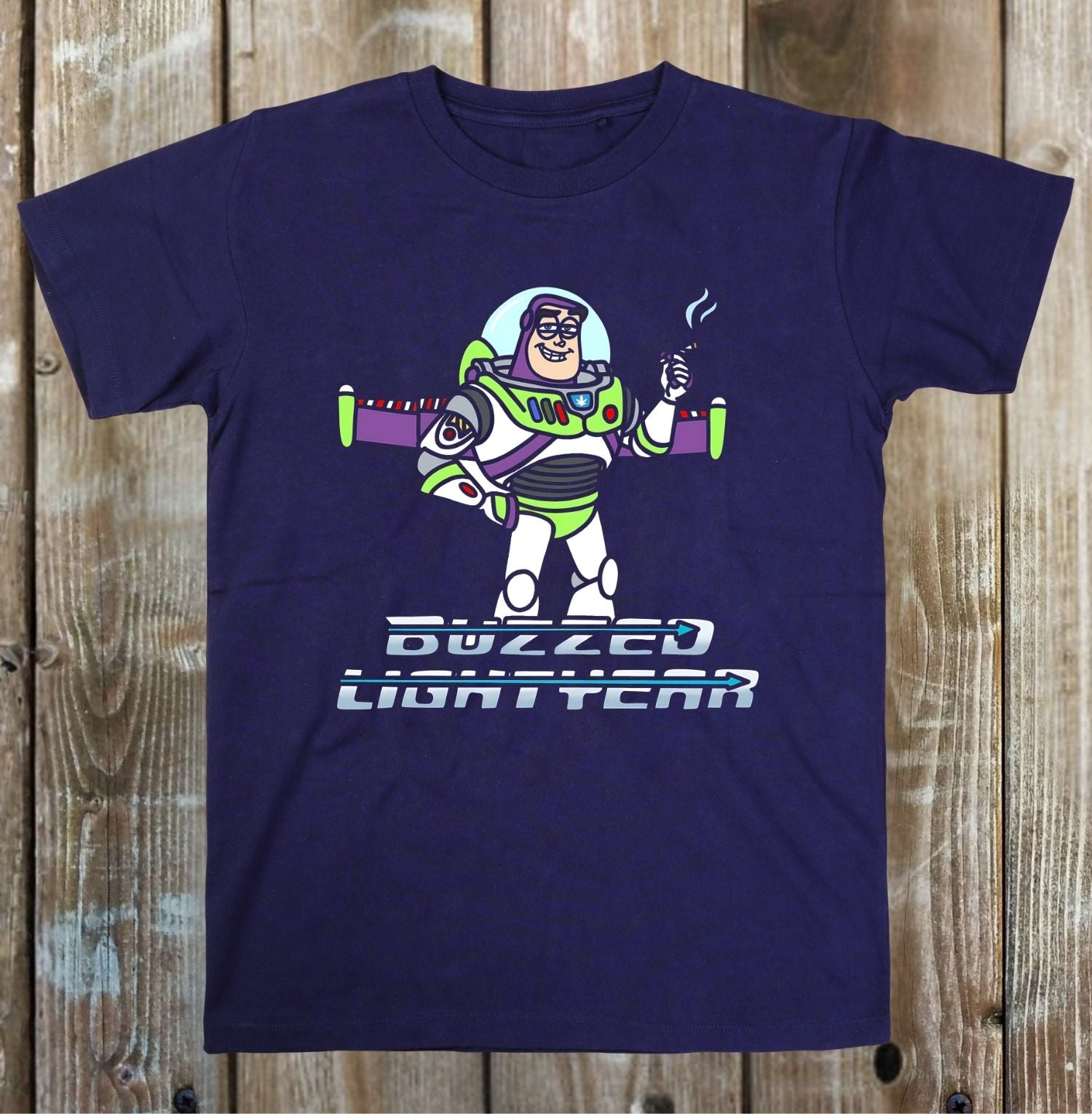 A navy blue crewneck t-shirt featuring a cartoon graphic of Buzz Lightyear smoking a cigar with the text 'BUZZED LIGHTYEAR' underneath, displayed flat against a rustic wooden plank background.