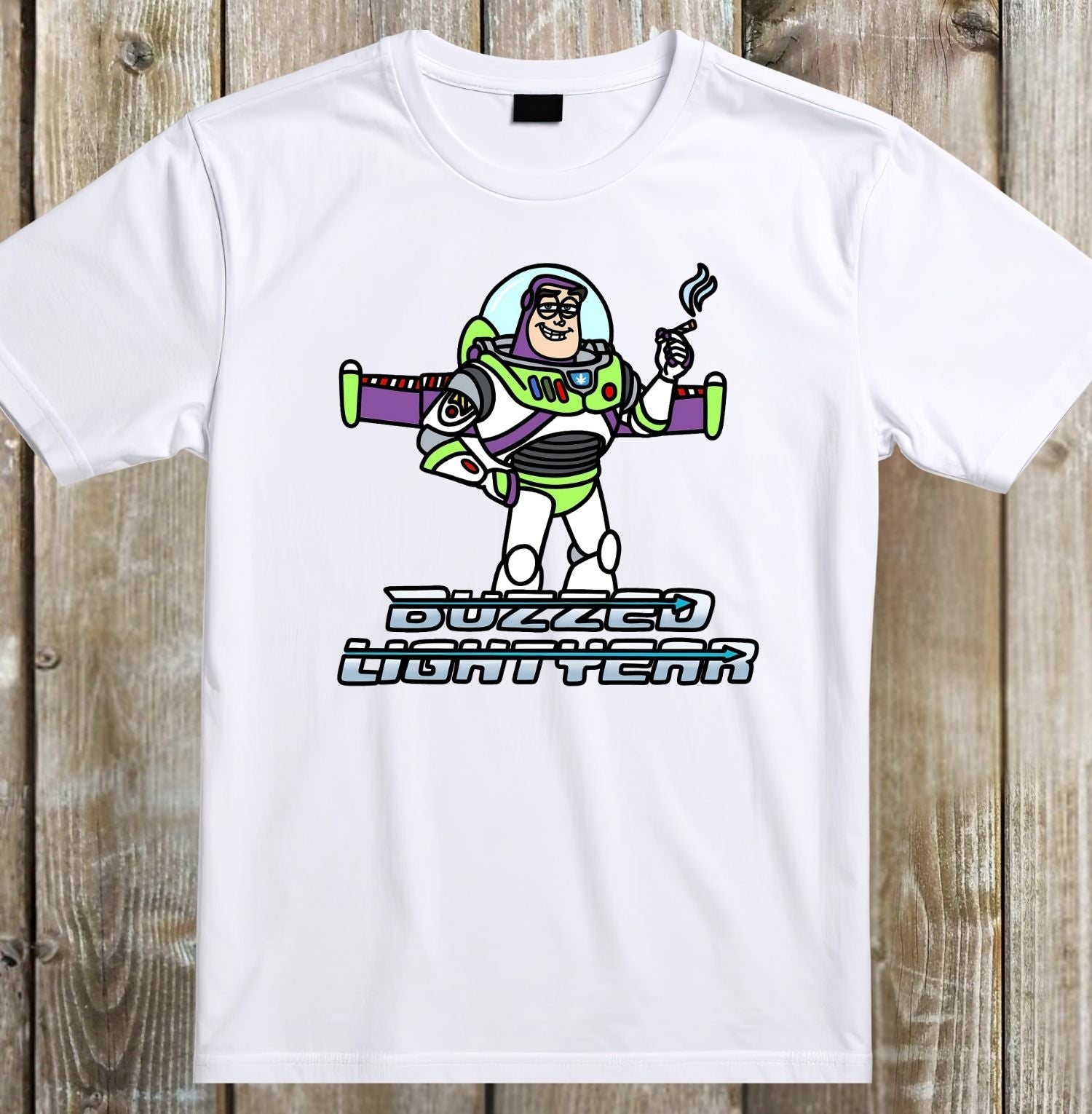 A white short-sleeve crewneck t-shirt featuring a cartoon graphic of Buzz Lightyear holding a cigarette with the text 'BUZZED LIGHTYEAR' underneath, displayed flat against a rustic wooden plank background.