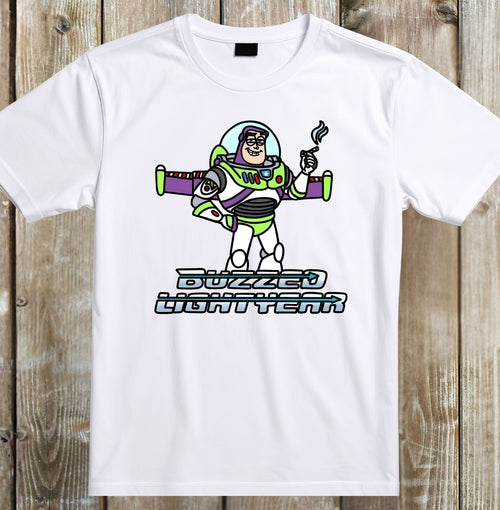 A white short-sleeve crewneck t-shirt featuring a cartoon graphic of Buzz Lightyear holding a cigarette with the text 'BUZZED LIGHTYEAR' underneath, displayed flat against a rustic wooden plank background.
