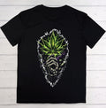 A black short-sleeve t-shirt laid flat on a white wood plank background, featuring a large graphic print of a smoking cannabis leaf in vibrant green and purple tones, with a skeletal hand holding the leaf.