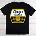 A black short-sleeve t-shirt laid flat on a white wood plank background, featuring a large graphic print on the front with the words 'Chingon Extra' and additional Spanish text in yellow and white.
