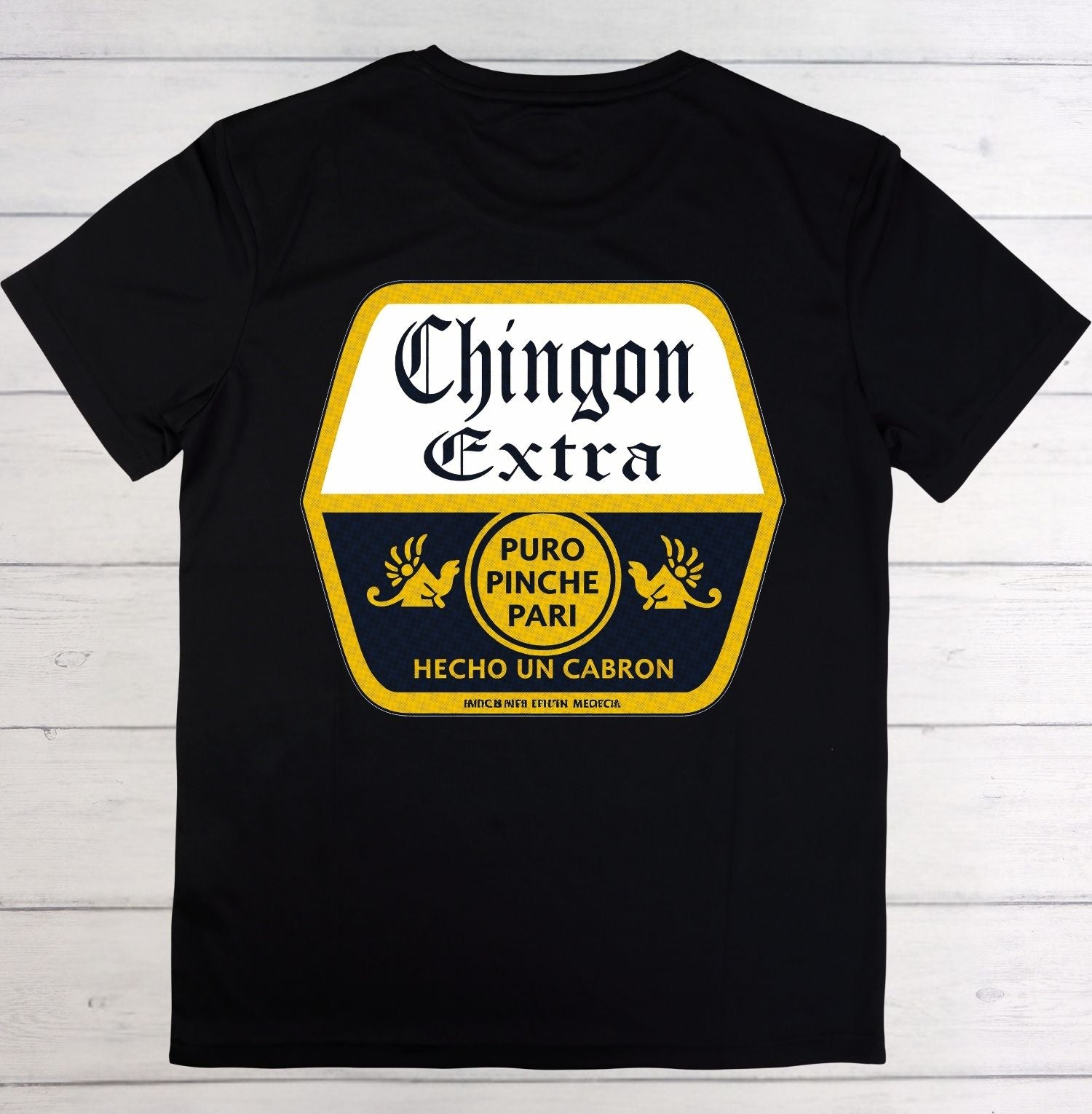 A black short-sleeve t-shirt laid flat on a white wood plank background, featuring a large graphic print on the front with the words 'Chingon Extra' and additional Spanish text in yellow and white.