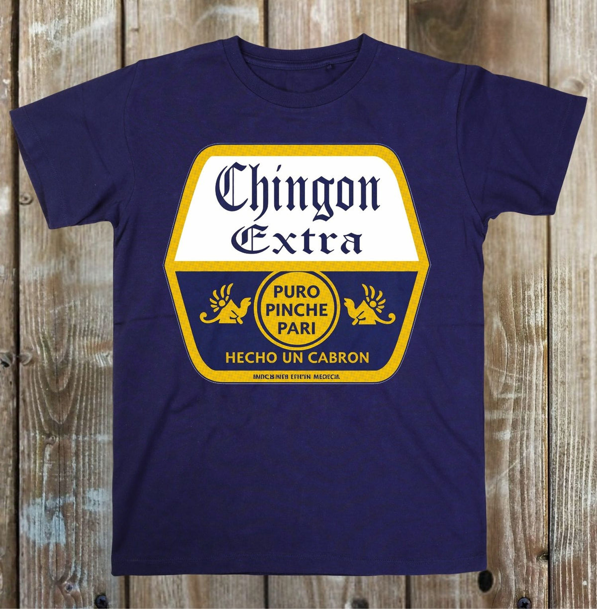 A navy blue short-sleeve t-shirt with a large vintage-style graphic on the chest. The graphic features a white and yellow shield-like shape with the text 'Chingon Extra', 'PURO PINCHE PARI', and 'HECHO UN CABRON' in navy and yellow lettering.