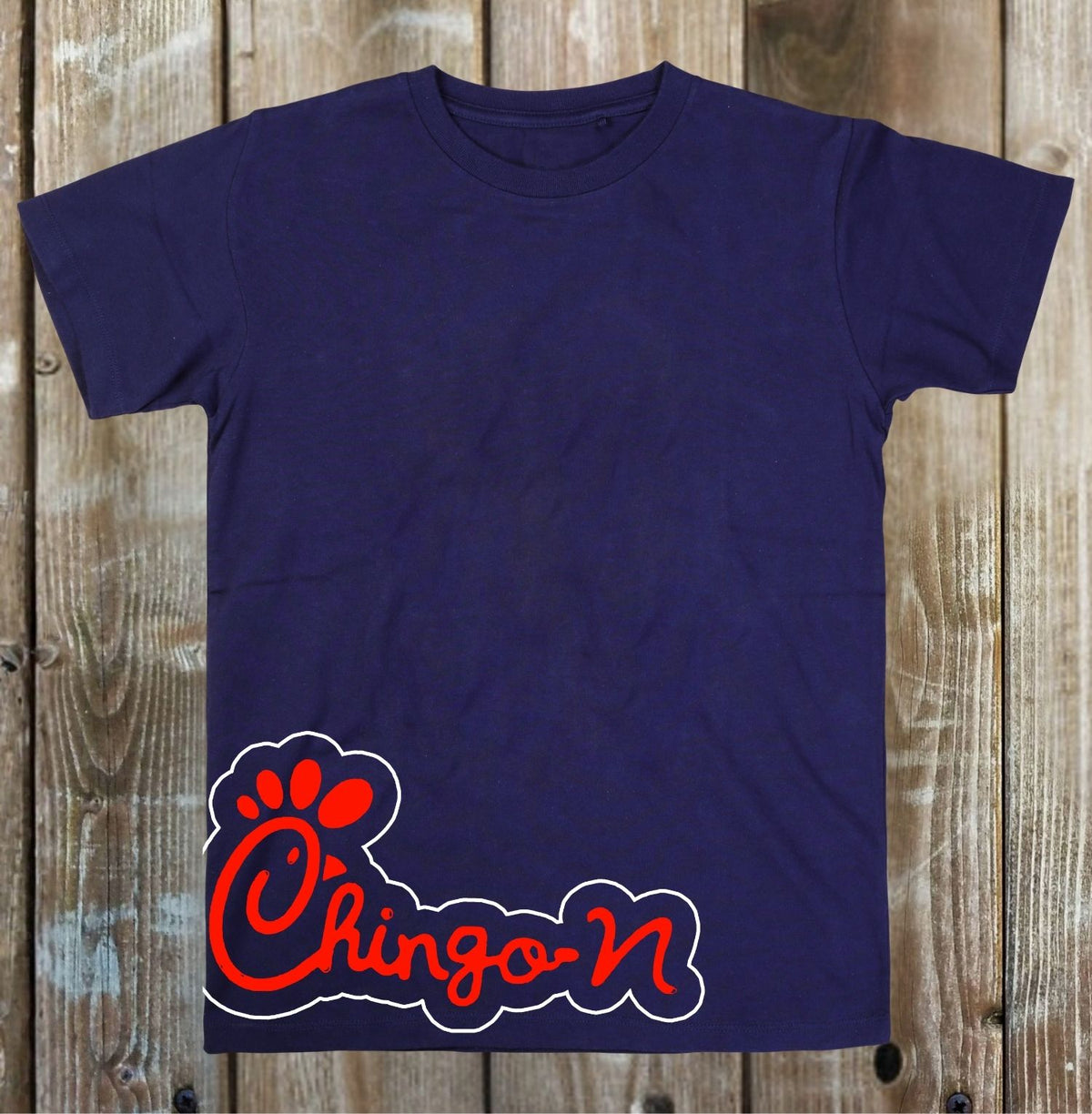 A navy blue short-sleeve t-shirt with a red and white 'Chingo-N' paw print graphic on the front, displayed flat against a rustic wooden plank background.