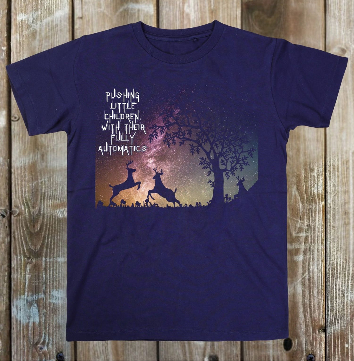 A navy blue short-sleeve t-shirt with a graphic print of two jumping deer silhouettes against a starry night sky and a tree, with the text 'PUSHING LITTLE CHILDREN WITH THEIR FULLY AUTOMATIC.' printed in white.
