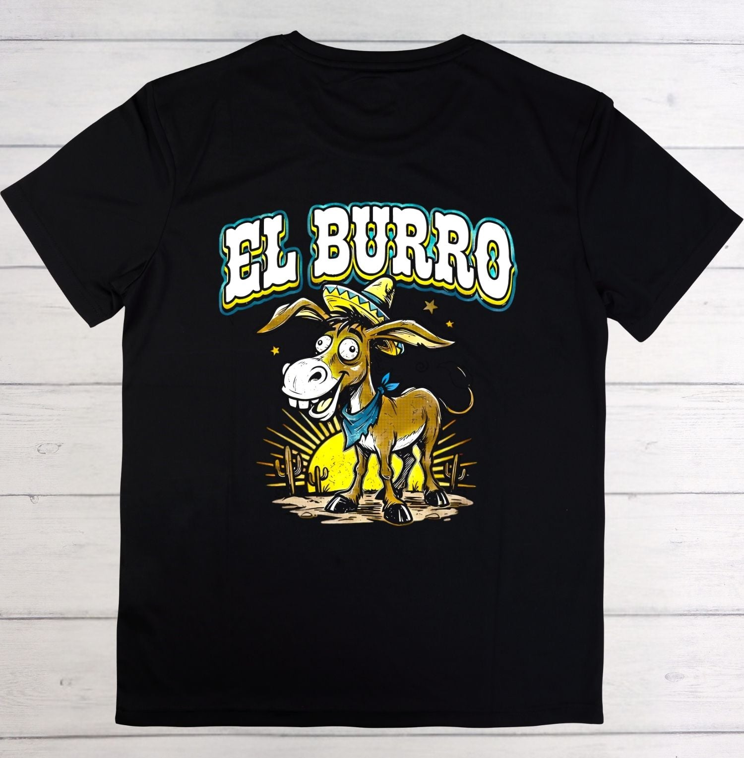 A black short-sleeve t-shirt laid flat on a white wood plank background, featuring a colorful graphic of a cartoon donkey wearing a sombrero and blue bandana beneath the text 'EL BURRO'.