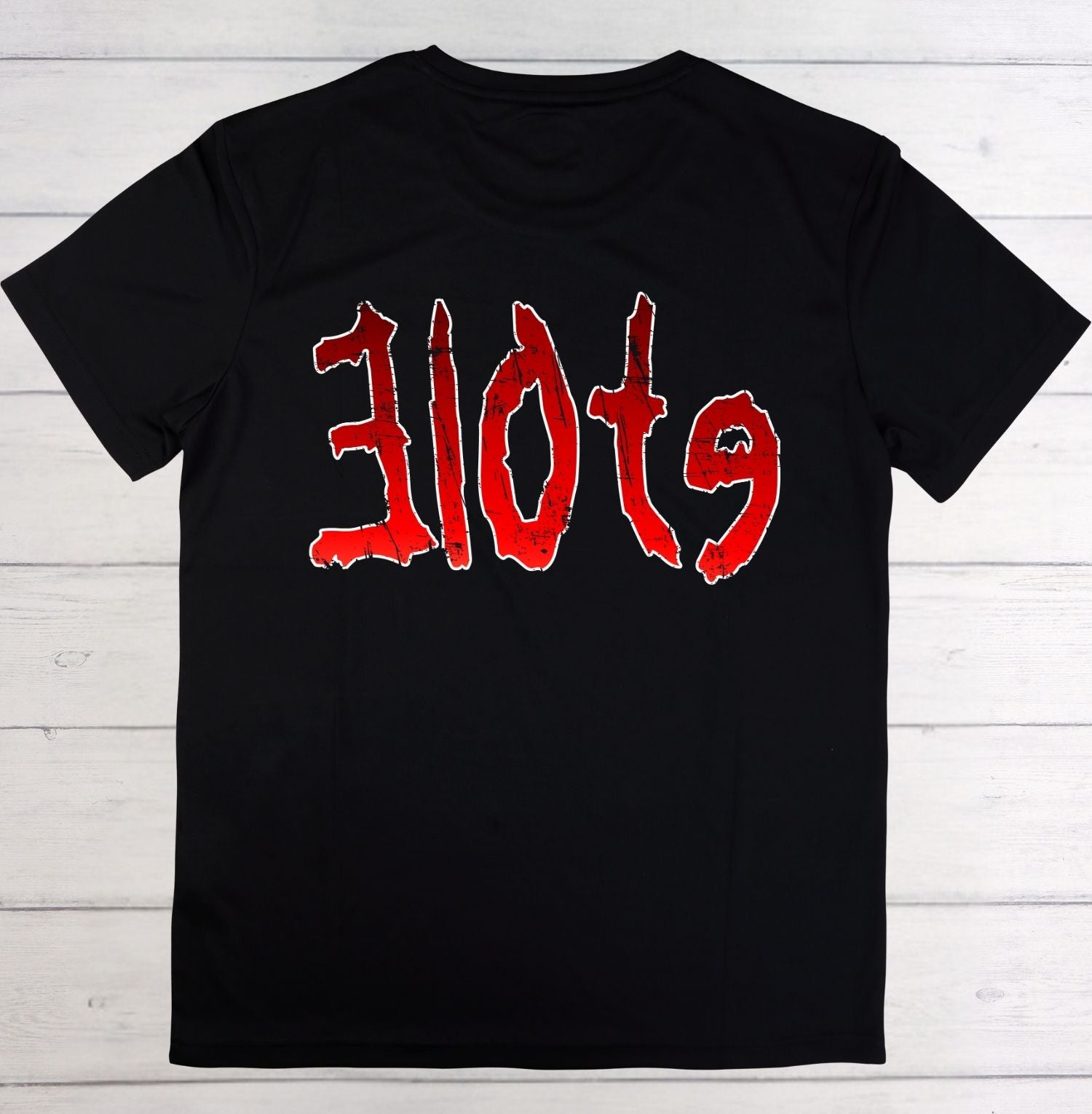 A black short-sleeve t-shirt with the word 'slots' printed across the chest in a stylized red font with a white outline, laid flat on a white wood plank background.