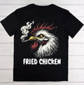 A black short-sleeve t-shirt laid flat on a white wood plank background, featuring a graphic of a smoking rooster with the words 'FRIED CHICKEN' printed below in white.