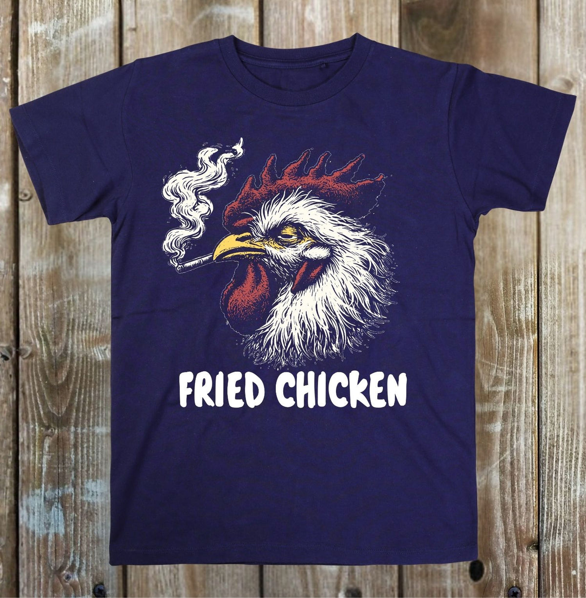 A navy blue short-sleeve t-shirt with a graphic of a smoking fried chicken rooster and the text 'FRIED CHICKEN' in white, displayed flat against a rustic wooden plank background.