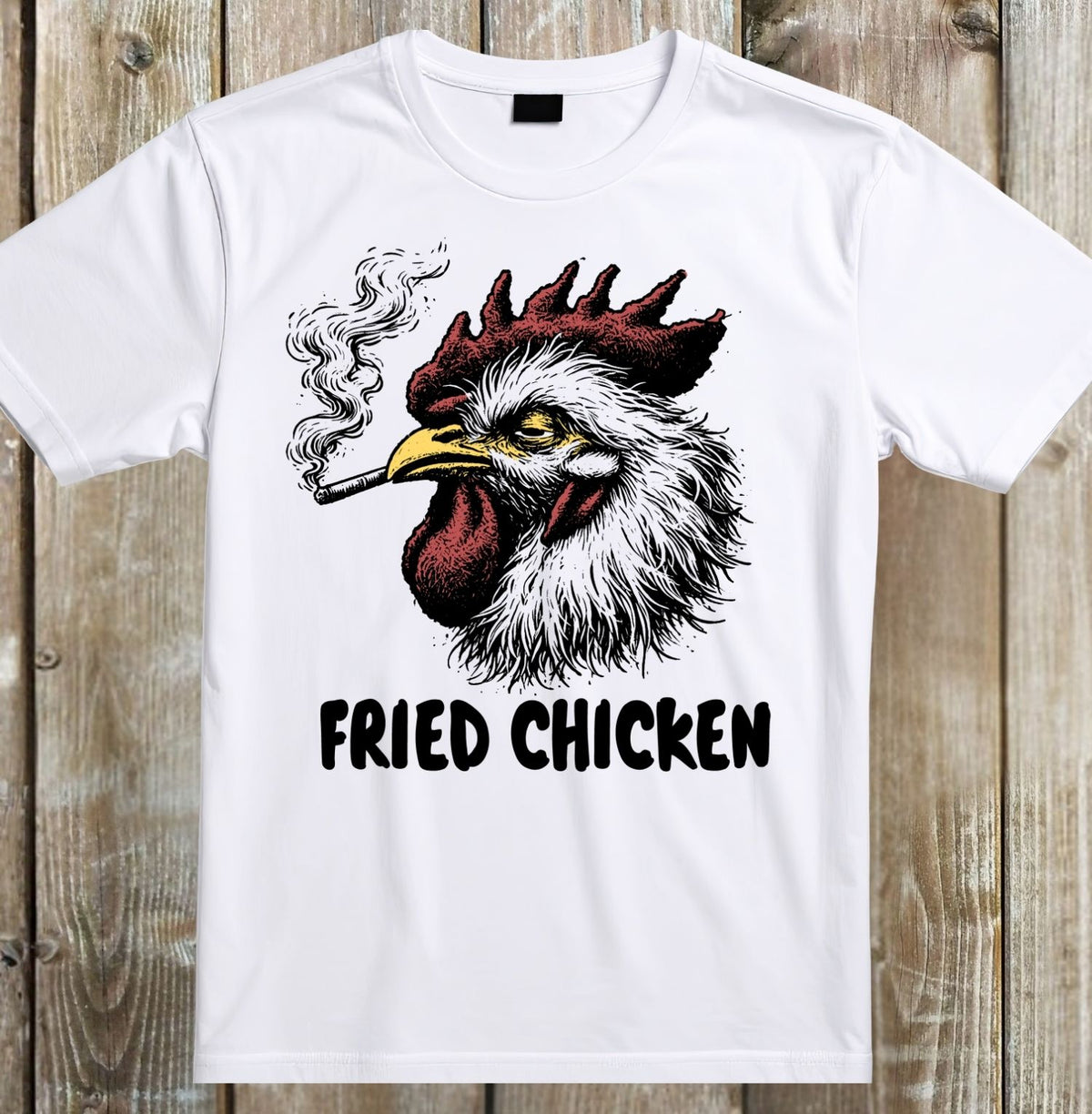 A white short-sleeve crewneck t-shirt laid flat on a rustic wooden plank background. The shirt features a graphic print of a smoking rooster with a red comb and wattle, and the text 'FRIED CHICKEN' printed below in black.