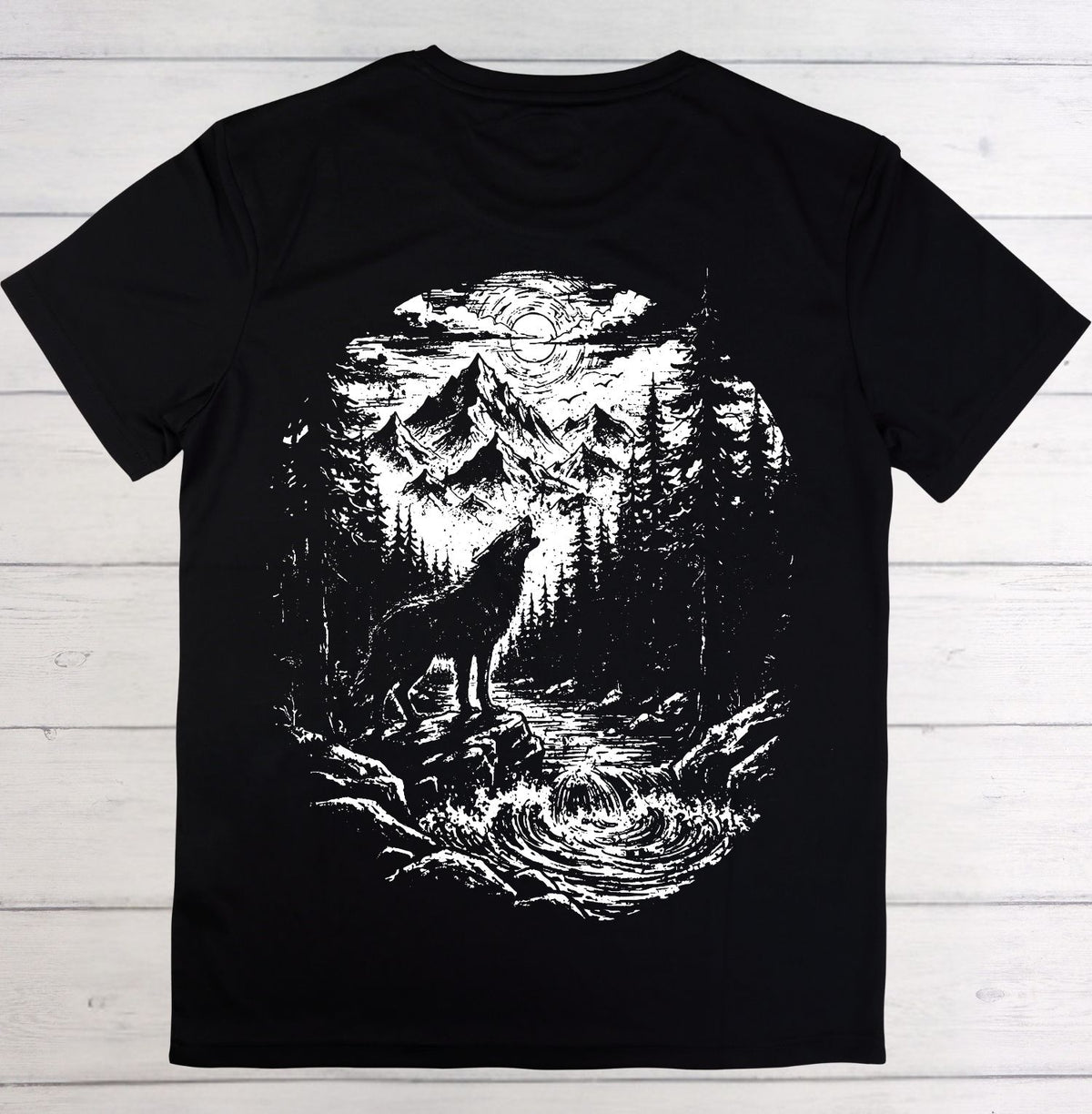 A black short-sleeve t-shirt laid flat on a white wood plank background, featuring a large white graphic print of a wolf howling in a forest by a river under a full moon.