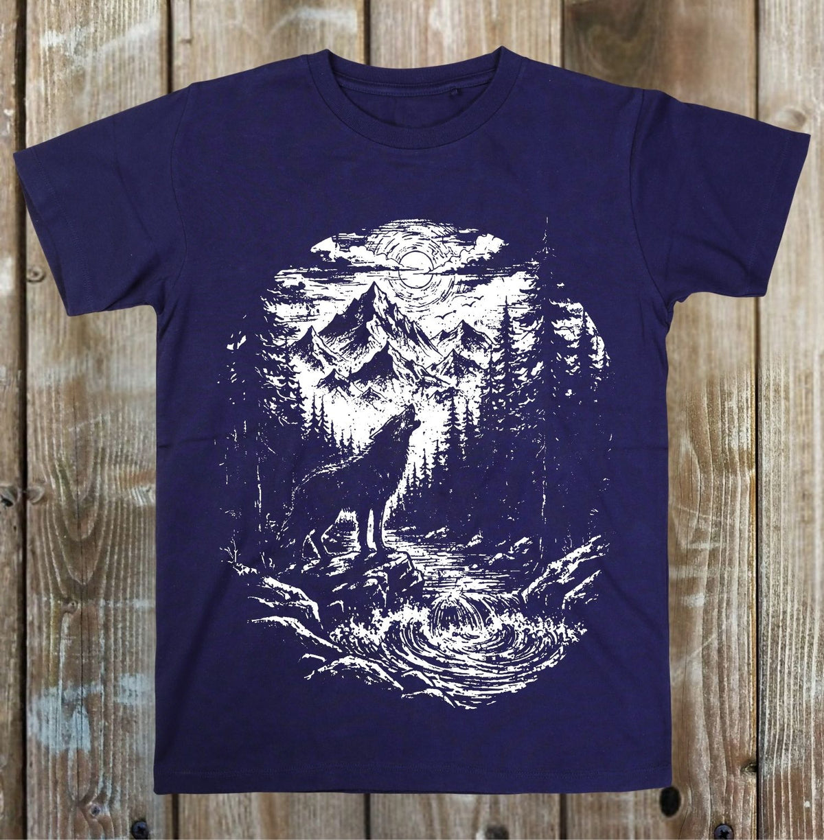 A navy blue short-sleeve t-shirt with a white distressed graphic print of a wolf howling at a mountain river, displayed flat against a rustic wooden plank background.