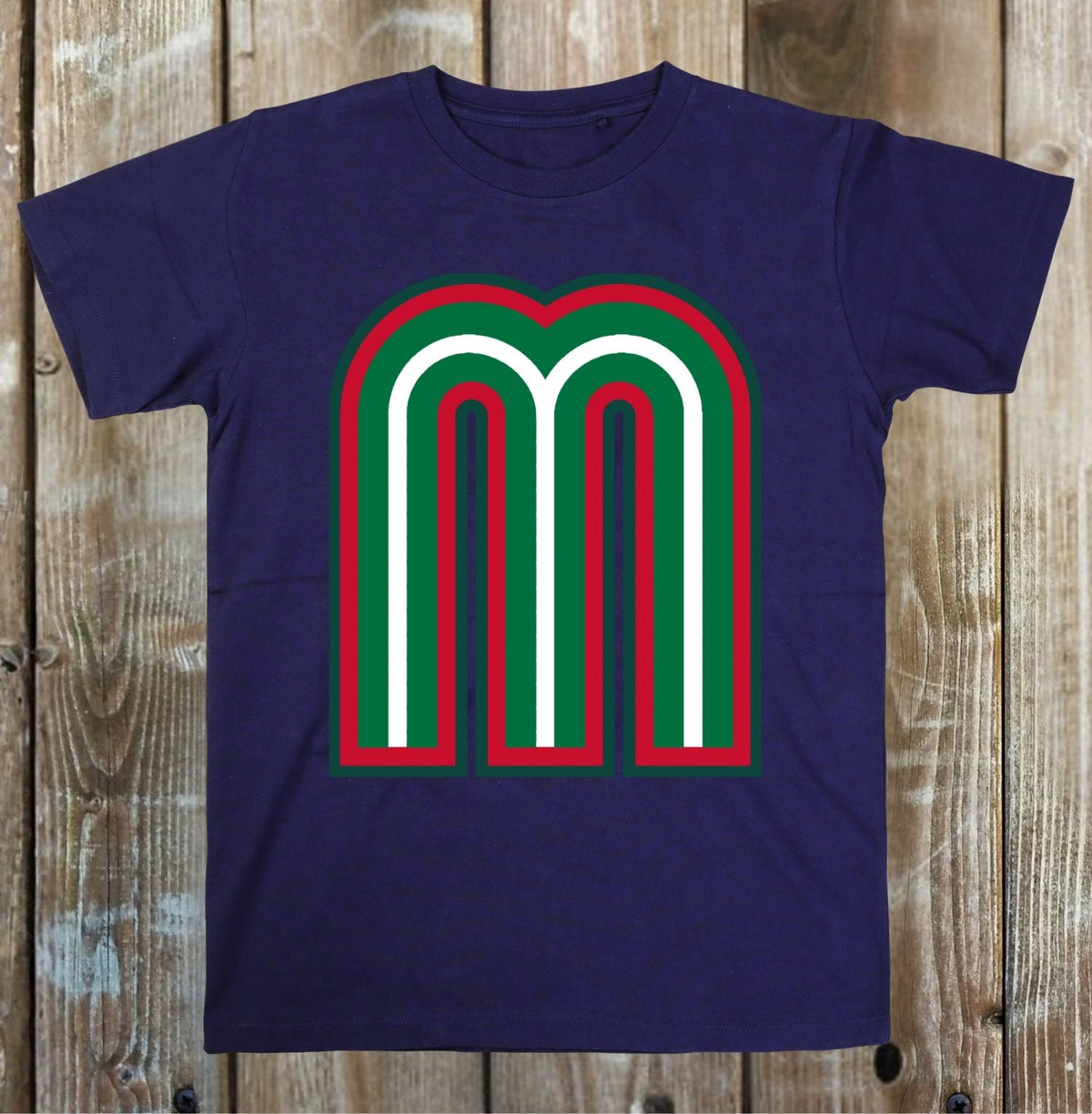 A navy blue short-sleeve t-shirt with a large graphic print of the letter 'm' in white, outlined in green and red, laid flat on a rustic wooden plank background.