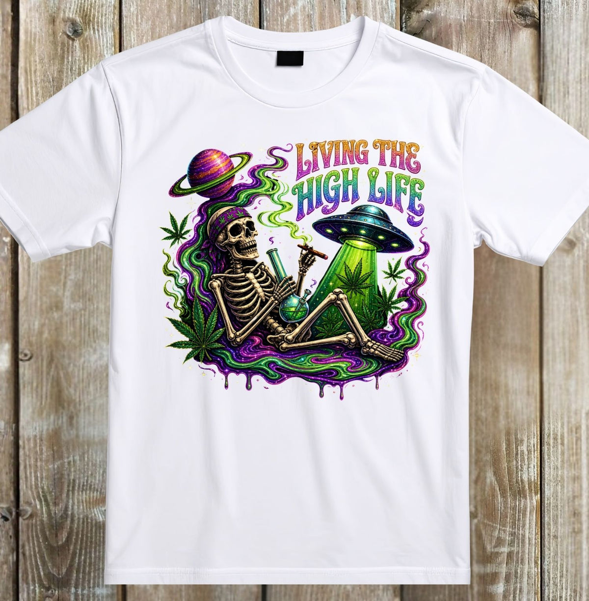 A white short-sleeve crewneck t-shirt with a colorful graphic print on the front, displayed flat against a rustic wooden plank background. The graphic features a skeleton smoking a green bong under a rainbow-colored planet and the text 'LIVING THE HIGH LIFE'.