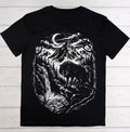 A black short-sleeve t-shirt laid flat on a white wood plank background, featuring a large white graphic print of a wolf in a forest under a crescent moon.