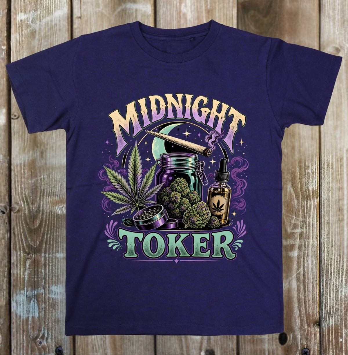A blue short-sleeve crewneck t-shirt with a colorful graphic print on the front, laid flat against a rustic wooden plank background. The graphic features the words 'MIDNIGHT TOKER' in stylized purple and green lettering, surrounding an illustration of a joint, a bong, a cannabis leaf, and a dropper bottle.