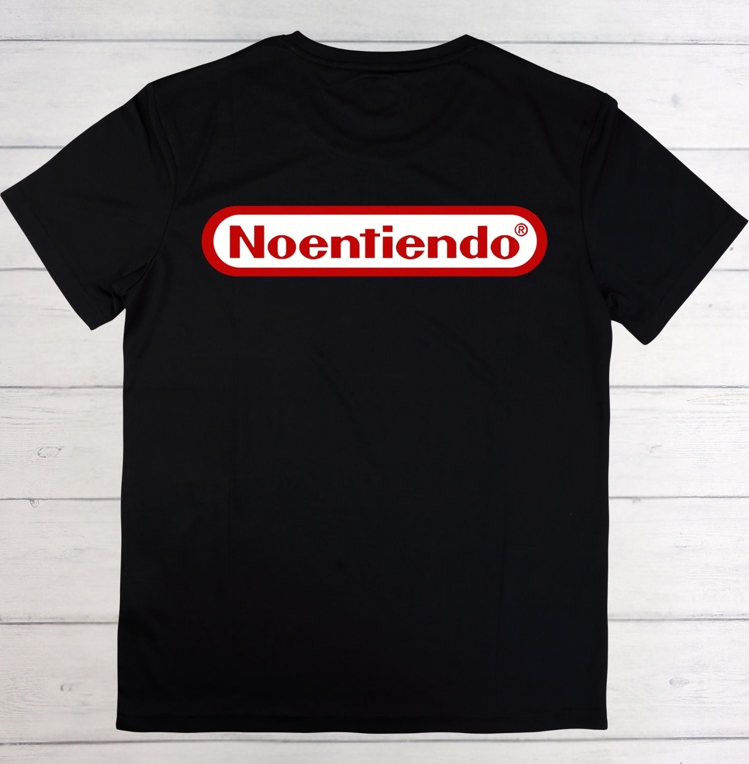 A black short-sleeve t-shirt laid flat on a white wood plank background, featuring a red and white 'Noentiendo' logo graphic across the chest.