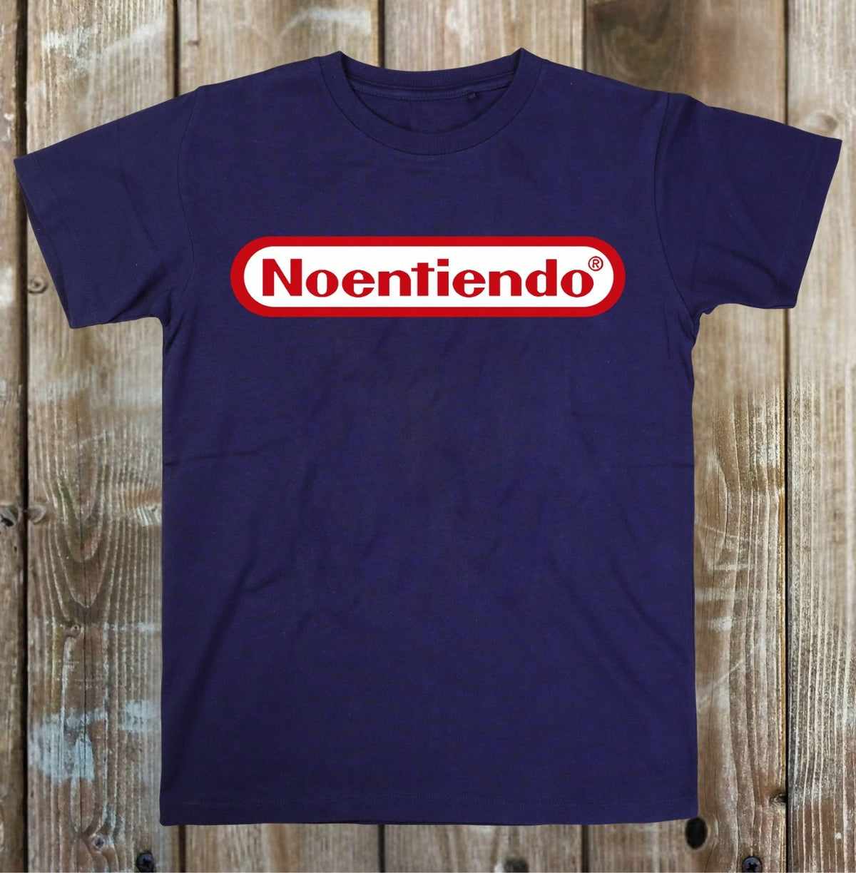 A navy blue short-sleeve t-shirt with a 'Noentiendo' logo graphic on the chest, laid flat on a rustic wooden plank background.