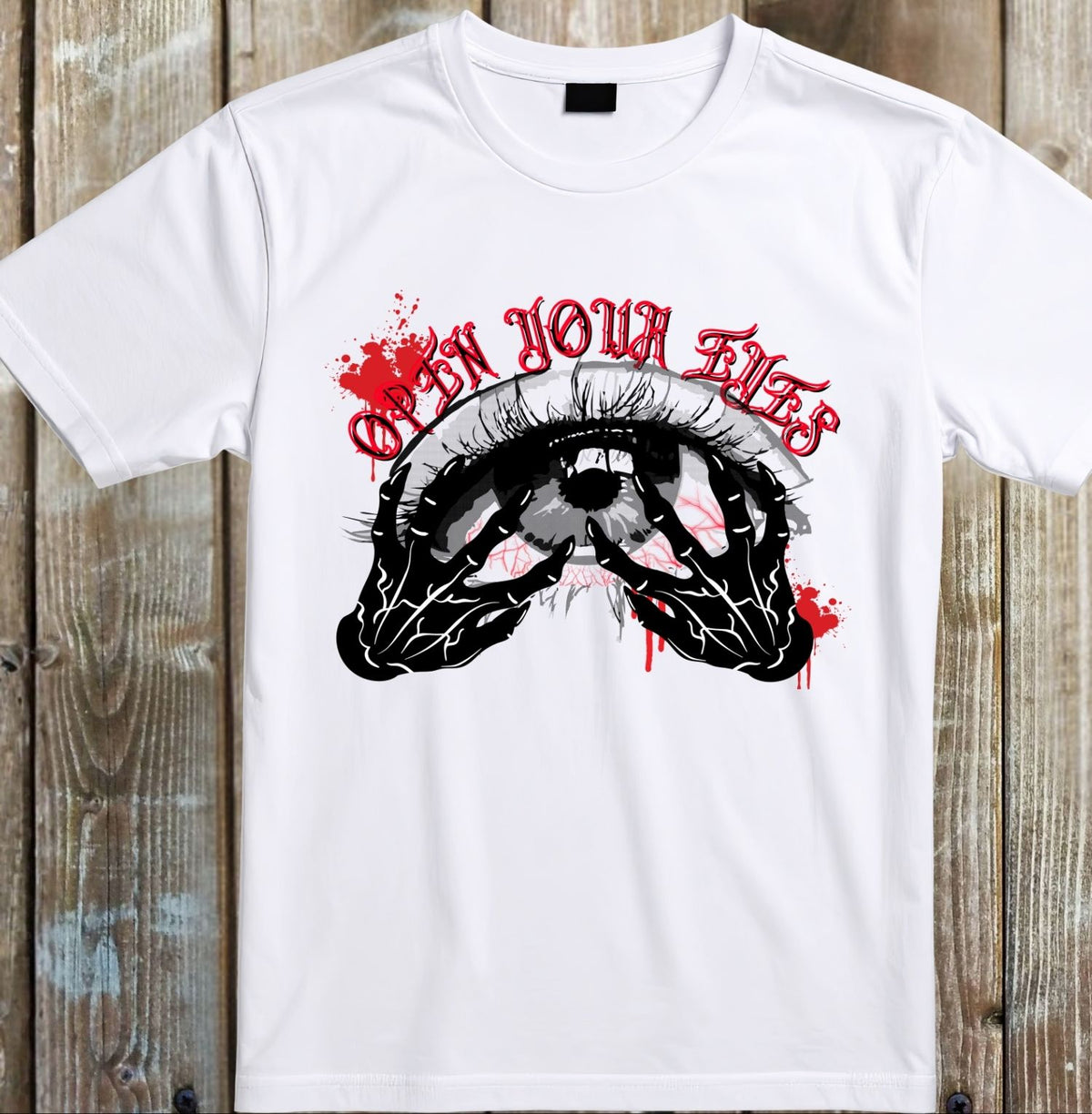 A white short-sleeve graphic t-shirt laid flat on a rustic wooden plank background. The shirt features a horror-style graphic of a skeletal hand holding a human eye, with red blood splatters and the gothic text 'OPEN YOUR EYES' in red above the graphic.