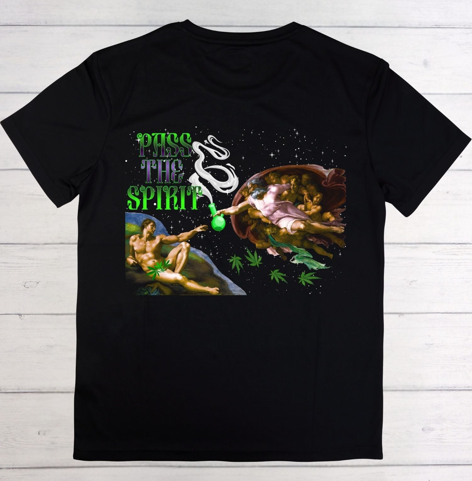 A black short-sleeve t-shirt with a detailed graphic print on the front, laid flat on a white wood plank background. The graphic features the text 'PUSH THE SPIRIT' in green and white, alongside a surreal illustration of a winged figure, a woman, and cannabis leaves.