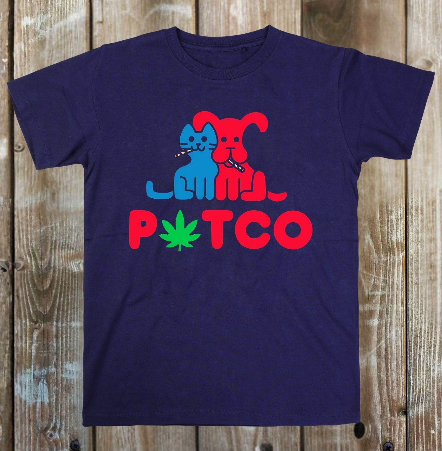 A navy blue short-sleeve t-shirt with a graphic print of a blue cat and a red dog smoking, with the word 'PTCO' in red and a green cannabis leaf in place of the letter 'T'. The shirt is displayed flat against a rustic wooden plank background.