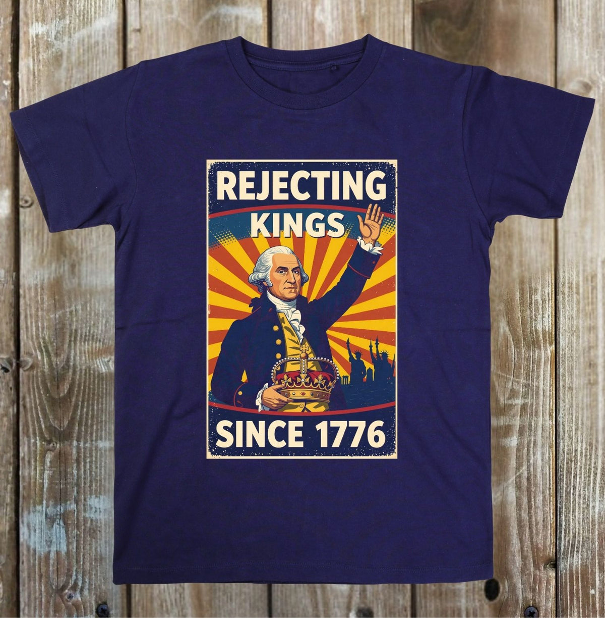 A navy blue short-sleeve t-shirt with a vintage-style graphic print of George Washington and the text 'REJECTING KINGS SINCE 1776' on a rustic wooden plank background.