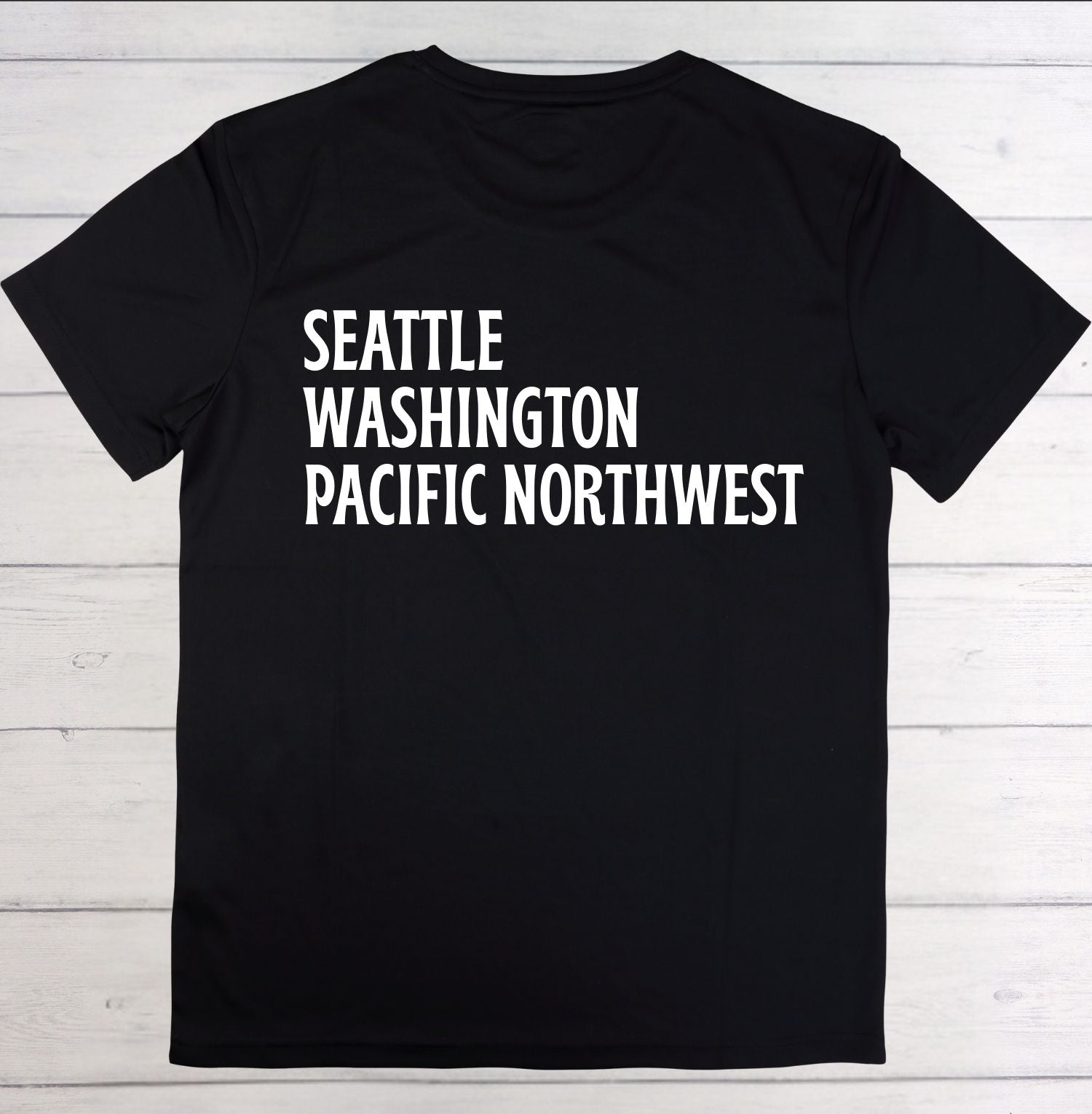 Black t-shirt with 'Seattle Washington Pacific Northwest' text on a wooden surface