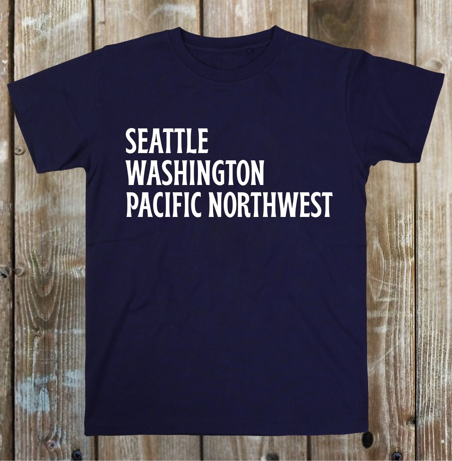 Navy blue t-shirt with 'Seattle Washington Pacific Northwest' text on a wooden background