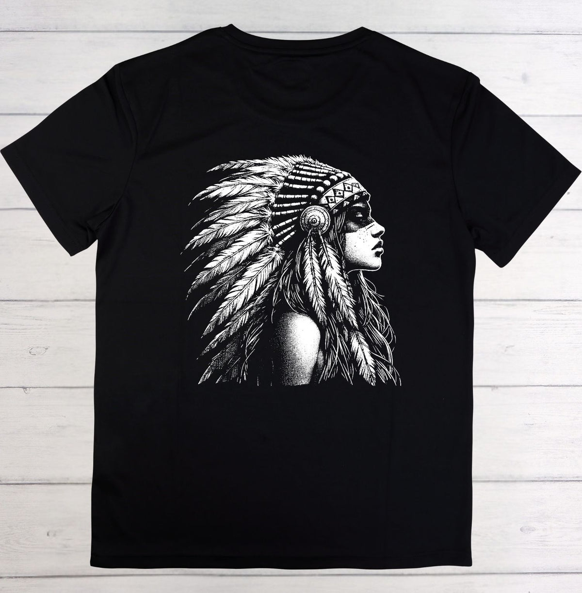 A black short-sleeve crewneck t-shirt featuring a detailed black and white graphic print of a woman in profile wearing a feathered headdress, laid flat on a light-colored wooden plank background.