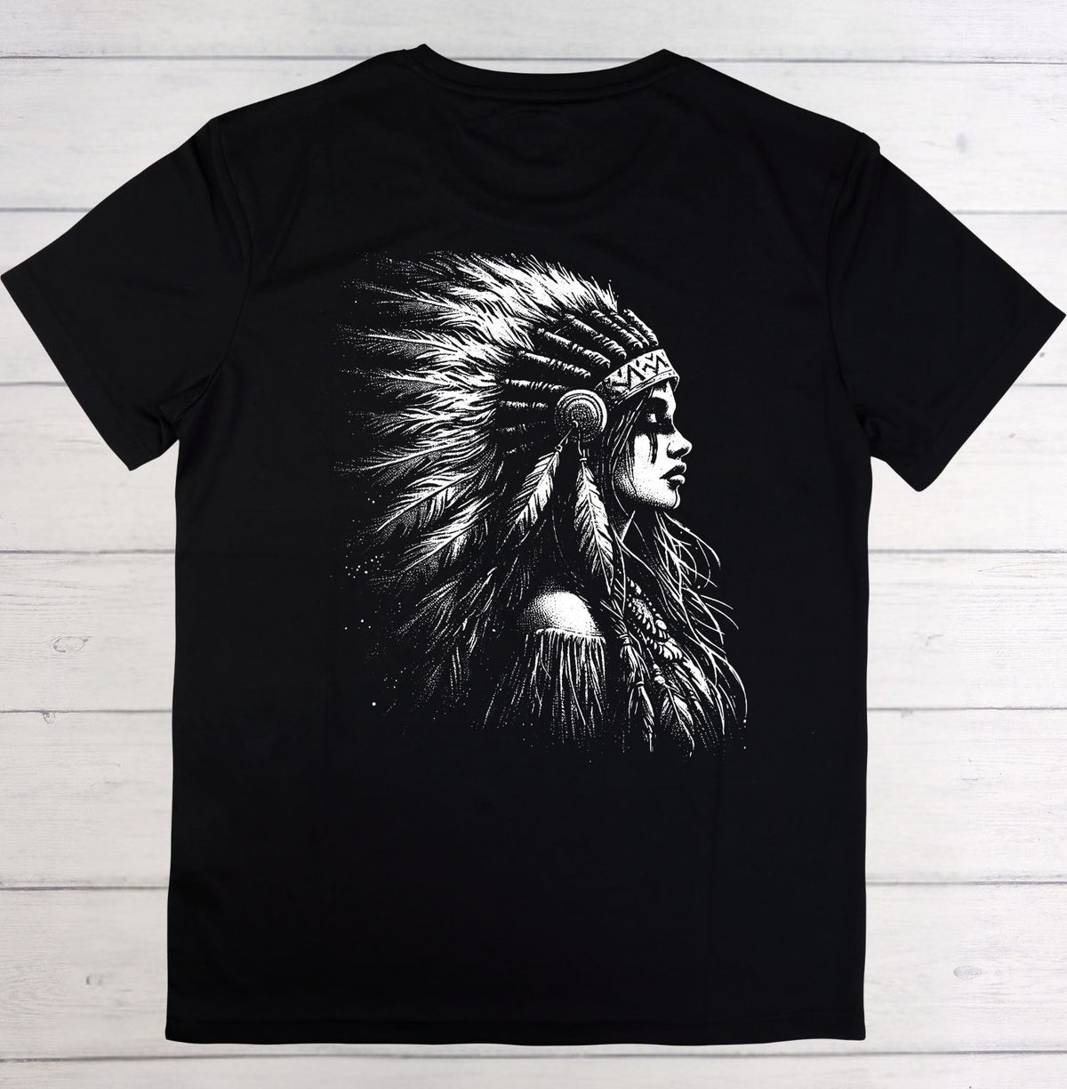 A black short-sleeve crewneck t-shirt featuring a large white graphic print of a woman in profile wearing a feathered headdress, laid flat on a light-colored wooden plank background.