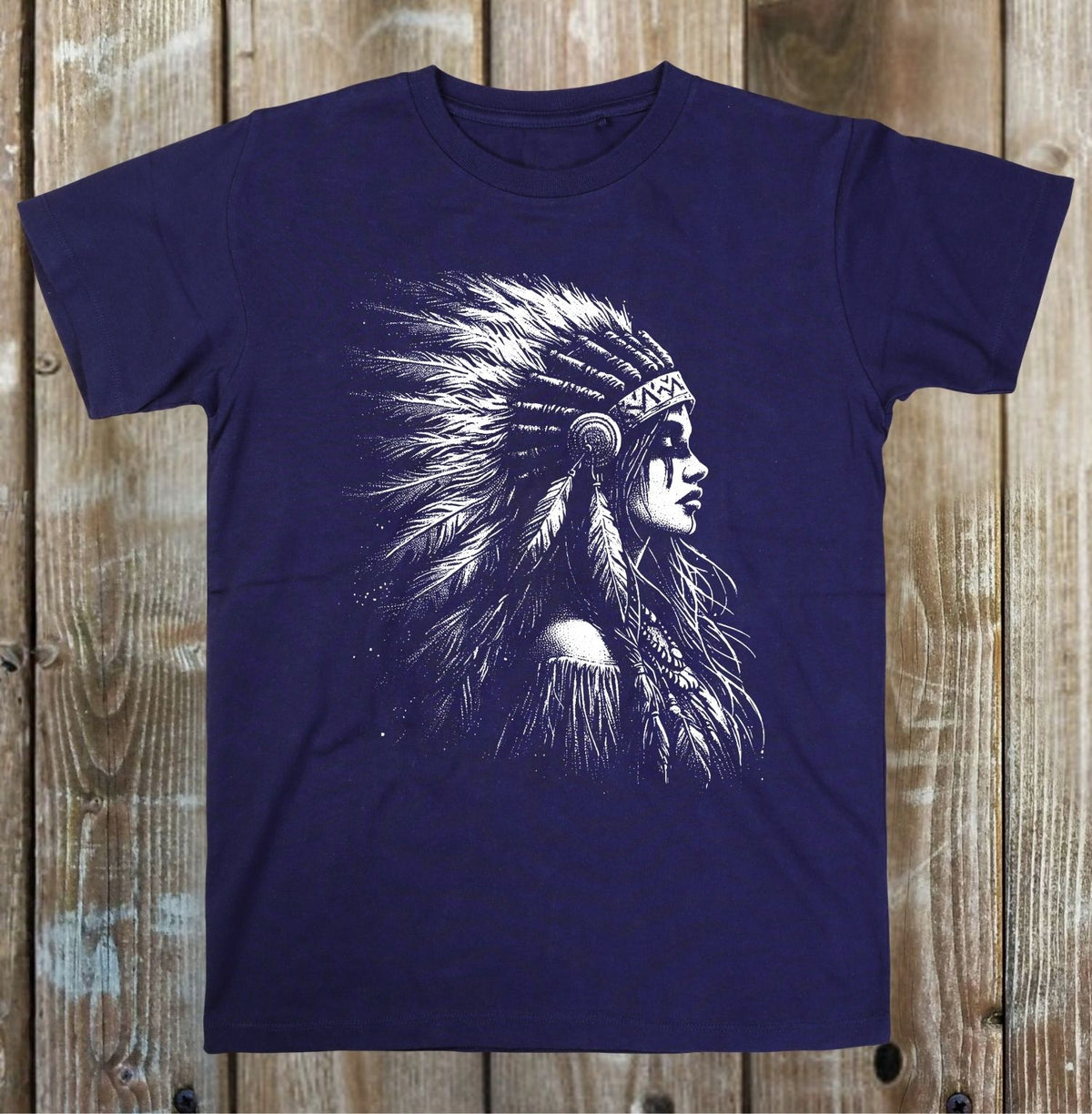 A navy blue short-sleeve t-shirt with a white graphic print of a Native American profile wearing a feathered headdress, displayed flat against a rustic wooden plank background.