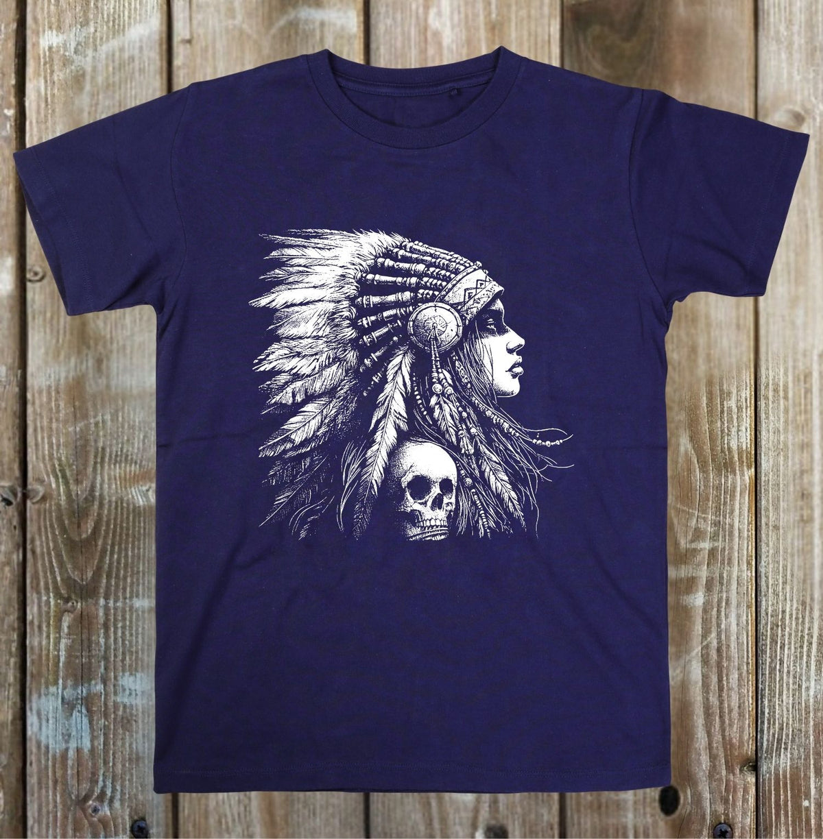 A navy blue short-sleeve t-shirt with a white graphic print of a Native American profile wearing a feathered headdress, displayed flat against a rustic wooden plank background.