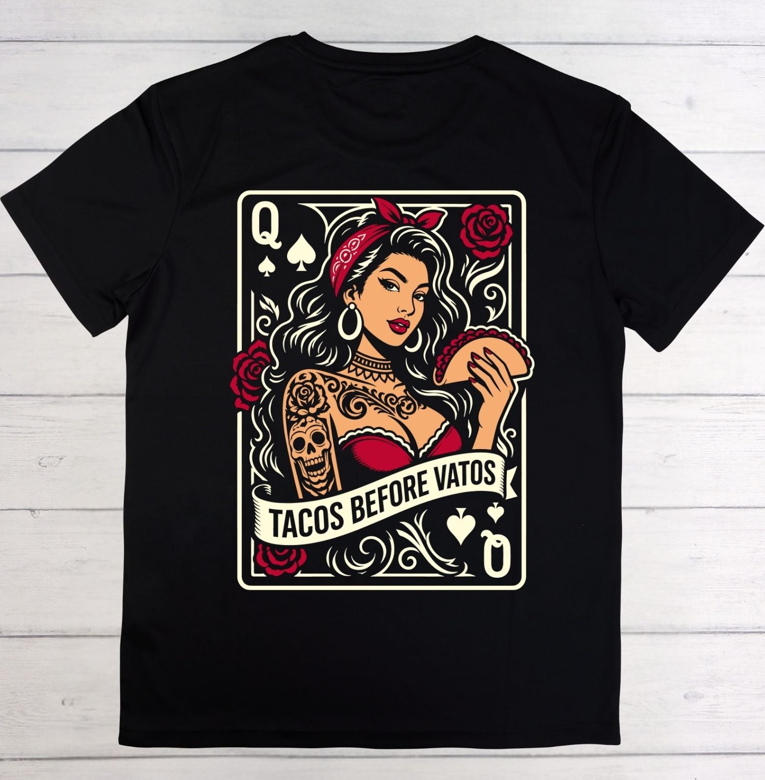 A black short-sleeve crewneck t-shirt laid flat on a white wood background, featuring a large graphic print of a Queen playing card illustration with a woman holding a taco and the text 'TACOS BEFORE VATOS'.