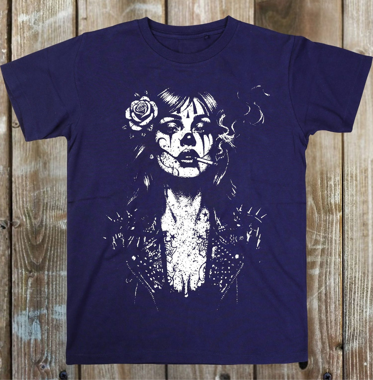 A dark navy blue short-sleeve t-shirt with a white distressed graphic of a gothic woman's face with a rose in her hair, laid flat on a rustic wooden plank background.