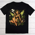 A black short-sleeve crewneck t-shirt laid flat on a white wood plank background, featuring a large graphic print of a female fairy with green wings, cannabis leaves, and white flowers.