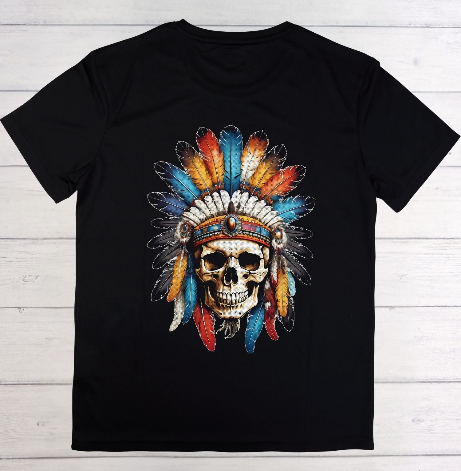 A black short-sleeve crewneck t-shirt laid flat on a white wood plank background, featuring a large graphic print of a skull wearing a colorful feathered headdress.