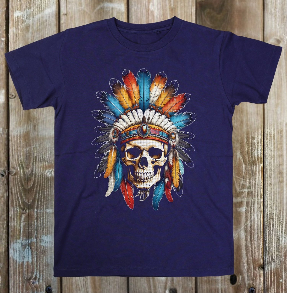 A navy blue short-sleeve t-shirt with a graphic of a skull wearing a colorful feathered headdress, displayed flat against a rustic wooden plank background.