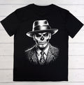 A black short-sleeve crewneck t-shirt featuring a detailed black and white graphic print of a skull wearing a fedora hat, pinstripe suit, and patterned tie, laid flat on a light-colored wooden plank background.