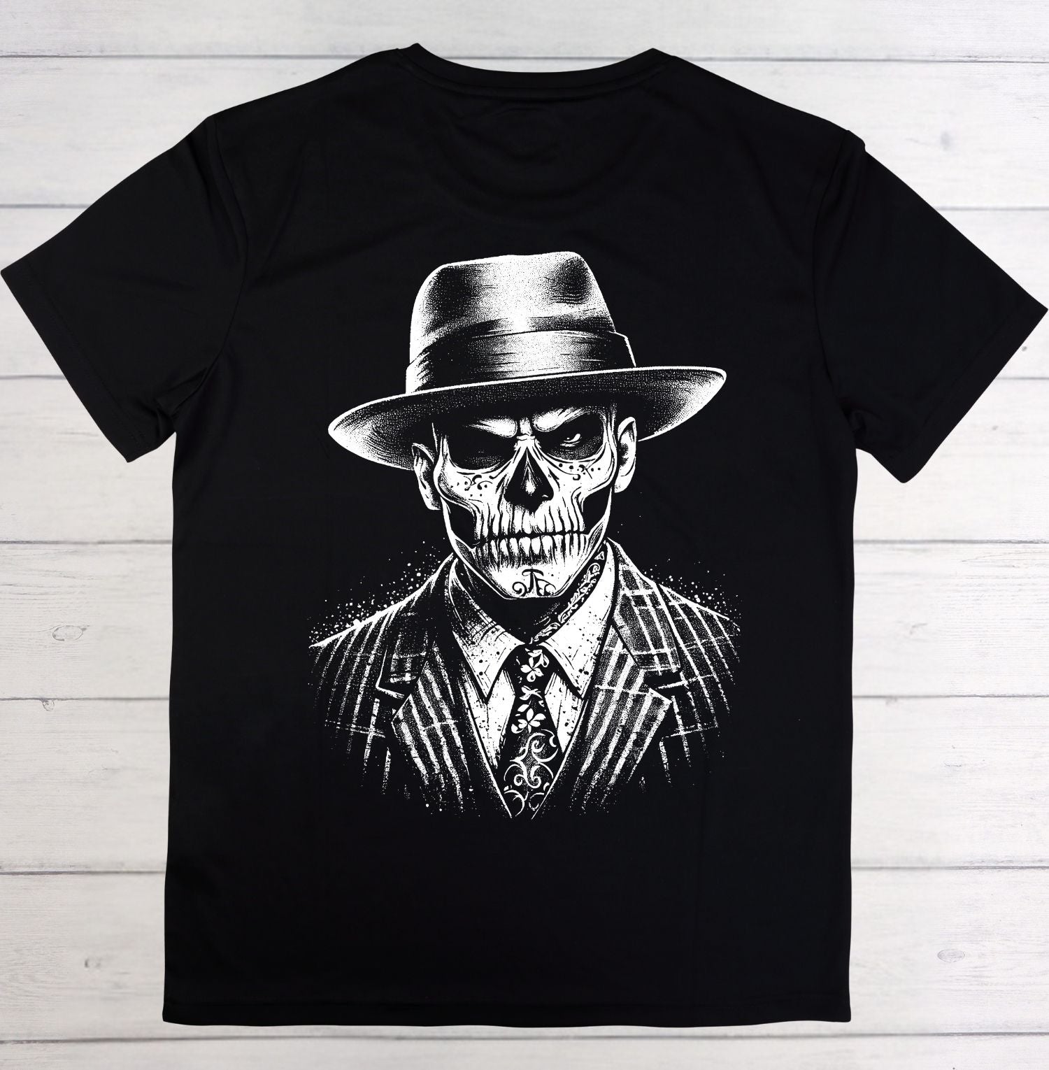 A black short-sleeve crewneck t-shirt featuring a detailed black and white graphic print of a skull wearing a fedora hat, pinstripe suit, and patterned tie, laid flat on a light-colored wooden plank background.