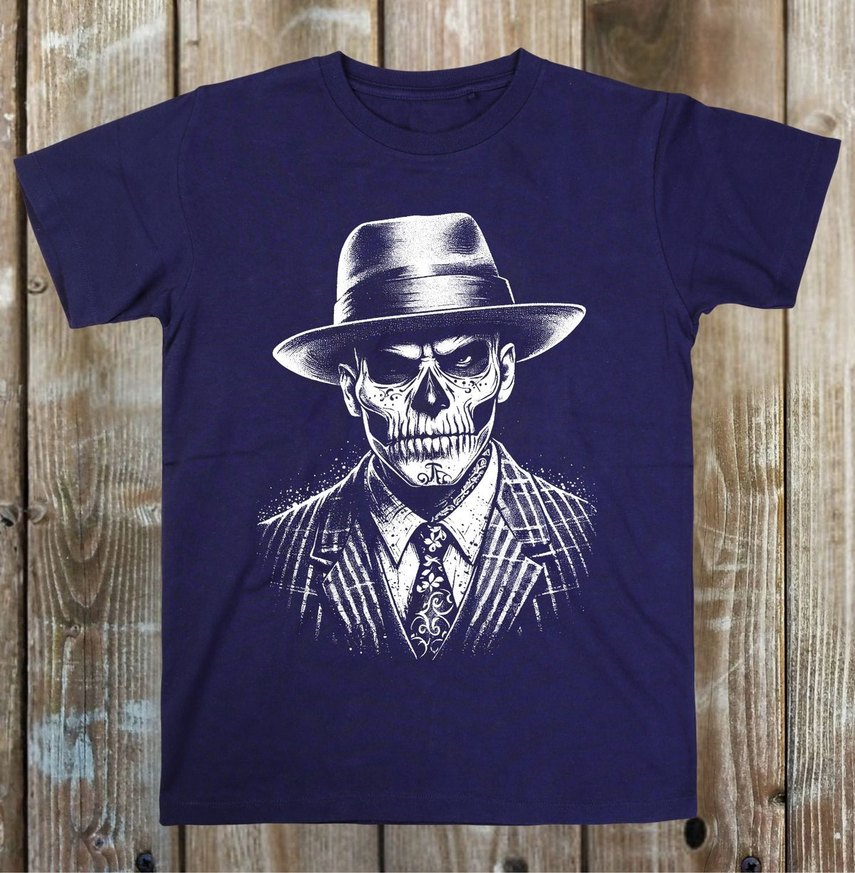 A navy blue short-sleeve t-shirt with a white graphic print of a skull in a fedora hat and pinstripe suit, displayed flat against a rustic wooden plank background.